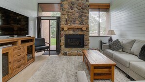 A living room with a stone fireplace, a television, a sofa, and a wooden coffee table. - Captain Molly 3 Bedroom Condo, Centrally Located in PC, Mins to Skiing! (Park City)