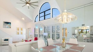 A spacious living area with a glass dining table, white sofas, and a large window with shutters. - Stunning Bay View's 3/2 home,10min Walk to beach (Fort Myers Beach)