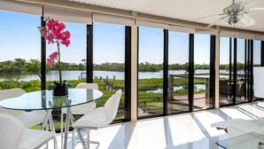A modern room with a glass table and chairs, large windows with a view of a lake and greenery. - Stunning Bay View's 3/2 home,10min Walk to beach (Fort Myers Beach)
