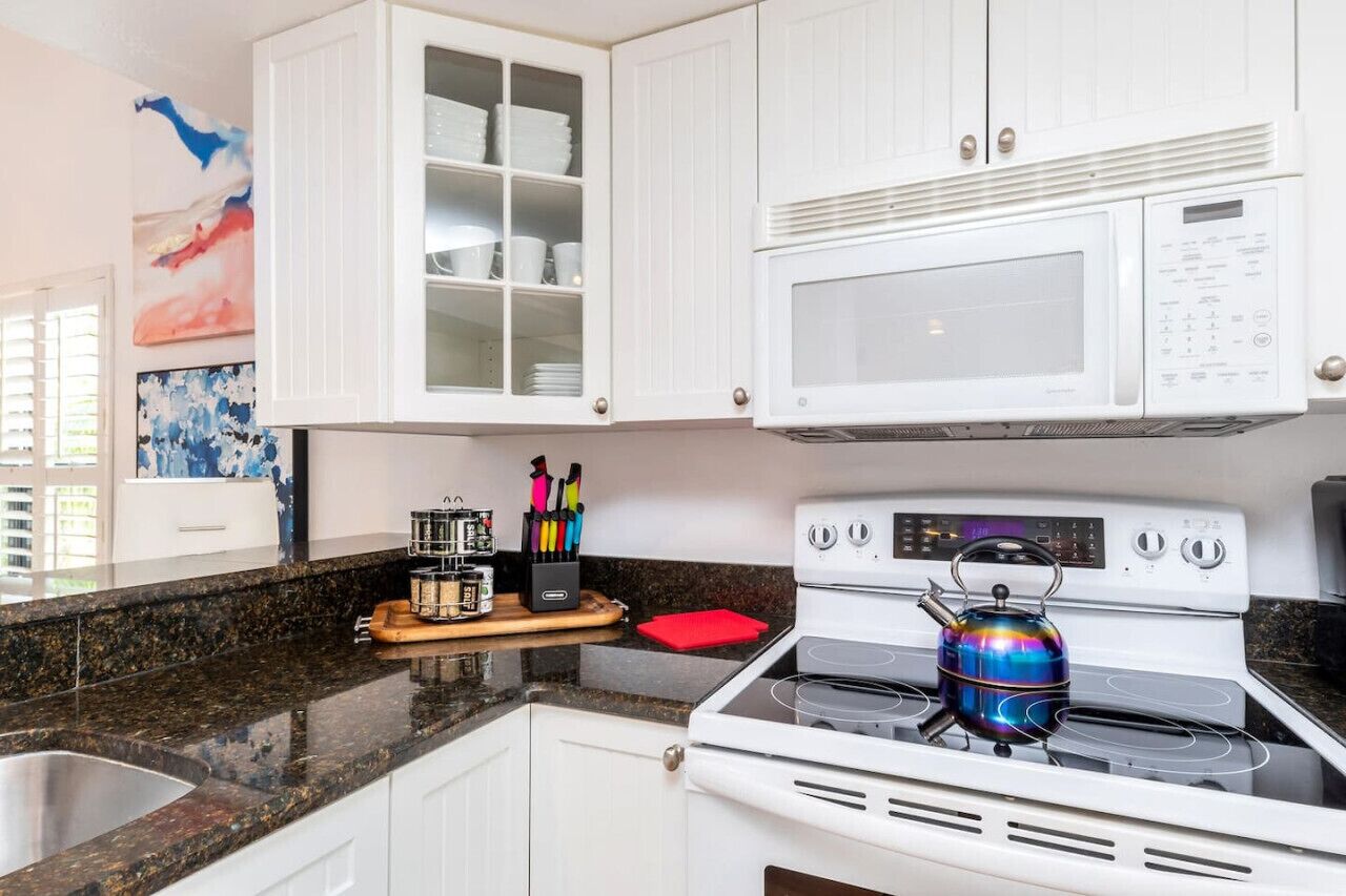 A kitchen with white cabinets, a microwave, a stove, and a colorful kettle.