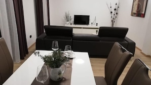 A modern living room with a sofa, a TV, and a dining table set with glasses and a plant. - Apartment in Duće with Seaview, Terrace, Air condition, WIFI (3423-6) (Duce)