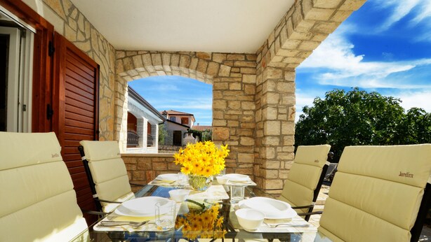 An outdoor patio with a glass table, white cushioned chairs, and a vase of yellow flowers. - Villa Bianca, Tar | Private Pool Villa in Istria (Rogovici)