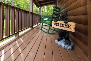 A wooden deck with a green rocking chair and a bear statue holding a 'WELCOME' sign. - Smoky Mtn Views! Hot Tub, Pool Table, Arcade Game. Resort Pool/Putt Putt/Fishing (Sevierville)