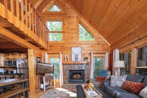 A wooden cabin interior with a dining area, kitchen, fireplace, and seating. - Smoky Mtn Views! Hot Tub, Pool Table, Arcade Game. Resort Pool/Putt Putt/Fishing (Sevierville)