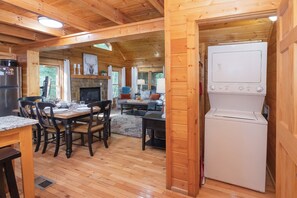 Interno di una baita in legno con zona pranzo, angolo cottura e un'ampia finestra.