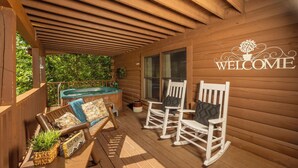 Une terrasse en bois avec une pancarte « BIENVENUE », des fauteuils à bascule, un banc et un jacuzzi.