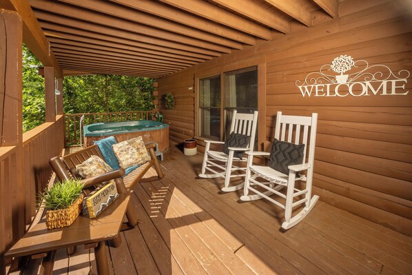 Un patio in legno con un cartello che dice 'WELCOME', poltrone a dondolo, una panchina e una vasca idromassaggio.