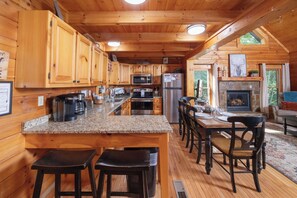 A wooden cabin interior with a kitchen, dining area, and fireplace. - Smoky Mtn Views! Hot Tub, Pool Table, Arcade Game. Resort Pool/Putt Putt/Fishing (Sevierville)