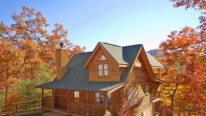 A log cabin with a porch, a chimney, and a mountain backdrop. - Great Mountain Views! 5miles to Pigeon Forge - Pool, Fishing, Putt Putt, Golf (Sevierville)