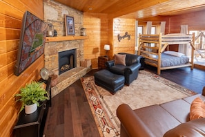 A cozy cabin interior with a fireplace, a sofa, a bunk bed, and a rustic wooden wall.