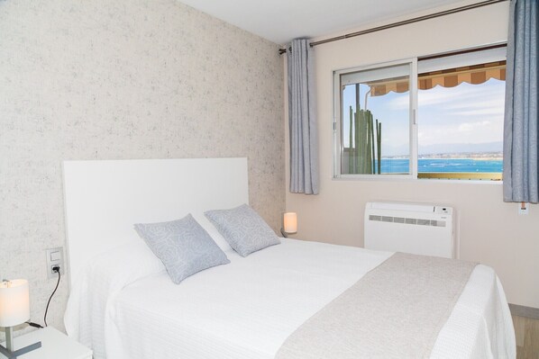 Une chambre à coucher avec un lit, une fenêtre donnant sur la mer et un climatiseur fixé au mur.