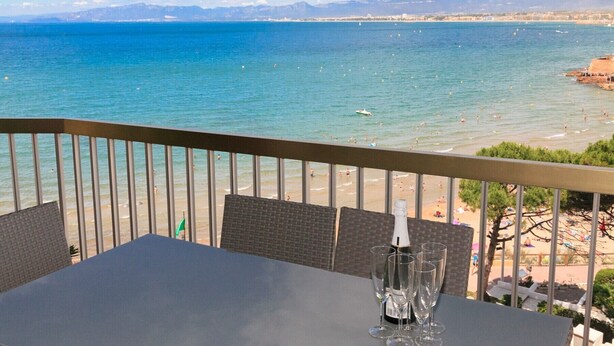 Un balcon avec une table et des chaises donnant sur une plage et la mer.