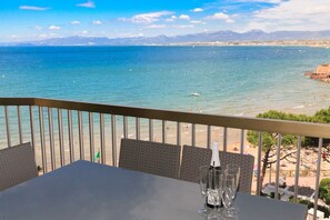 Un balcon avec une table et des chaises donnant sur une plage et la mer.