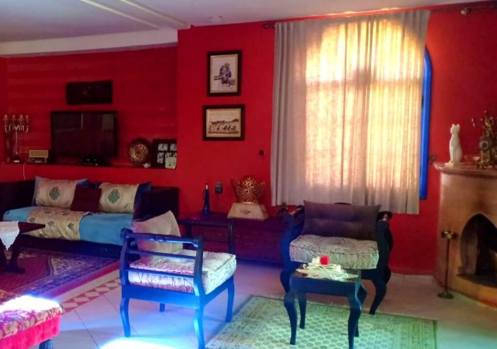 Een woonkamer met een rode wand, een bank, twee stoelen, een bijzettafeltje en een open haard.