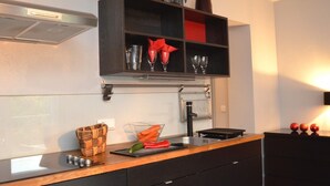 Une cuisine moderne avec un plan de travail noir, un four encastré et une étagère au-dessus pour ranger les ustensiles de cuisine.