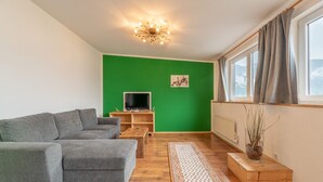 Un salón con pared verde, sofá gris, mesa de centro de madera y mueble para televisión.
