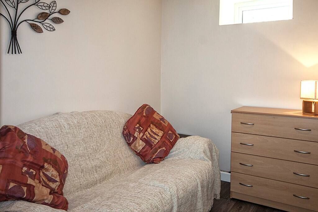 A cozy room with a beige sofa, a patterned throw pillow, and a wooden dresser with drawers.