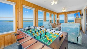 A room with wooden walls, large windows, a foosball table, and a sofa. - Soundfront Home w/ Private Boat Dock, Game Room, Windsports Access, & More! (Avon)