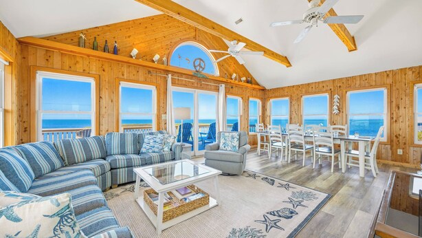 A spacious living area with a large sofa, a dining table, and multiple windows offering ocean views. - Soundfront Home w/ Private Boat Dock, Game Room, Windsports Access, & More! (Avon)