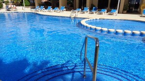 A swimming pool with a tiled edge, a metal ladder, and lounge chairs around the perimeter.