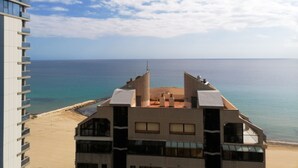 A modern building with a flat roof and multiple balconies overlooking a beach and the sea.
