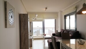 A modern living room with a glass dining table, a sofa, and a large window offering a view of the cityscape.