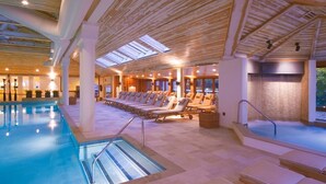 Ein Hallenbad mit sonnendurchfluteter Decke und Liegestühlen.