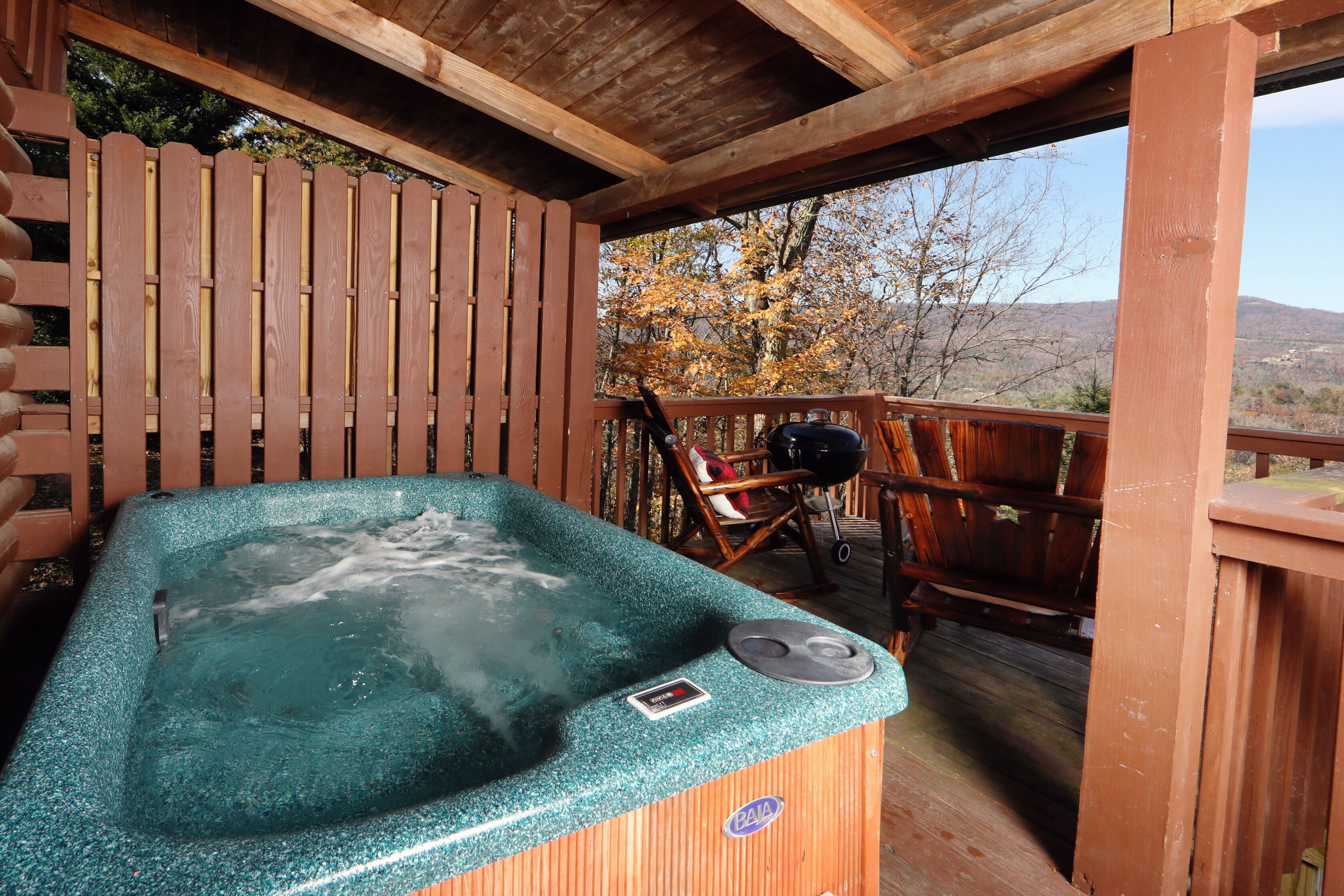 A hot tub on a wooden deck with a view of trees and hills.