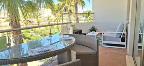 A balcony with a glass table, wicker furniture, and a view of a residential area with palm trees.