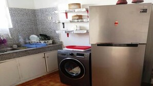 Eine kompakte Küche mit Waschmaschine, Edelstahlkühlschrank und Regalen mit Körben.