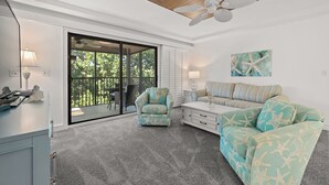 A spacious room with a large sliding glass door leading to a balcony, a ceiling fan, a striped sofa, and a starfish-patterned armchair.