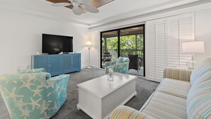 A living room with a flat-screen TV, blue cabinets, a white coffee table, striped sofas, and a ceiling fan.