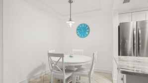 A small dining area with a round table and four chairs, a blue clock on the wall, and a modern kitchen with stainless steel appliances.