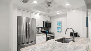 A modern kitchen with stainless steel appliances, a marble countertop, and a ceiling fan.