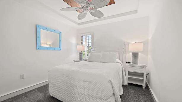 A bedroom with a bed, a nightstand, a lamp, a mirror, and a ceiling fan.