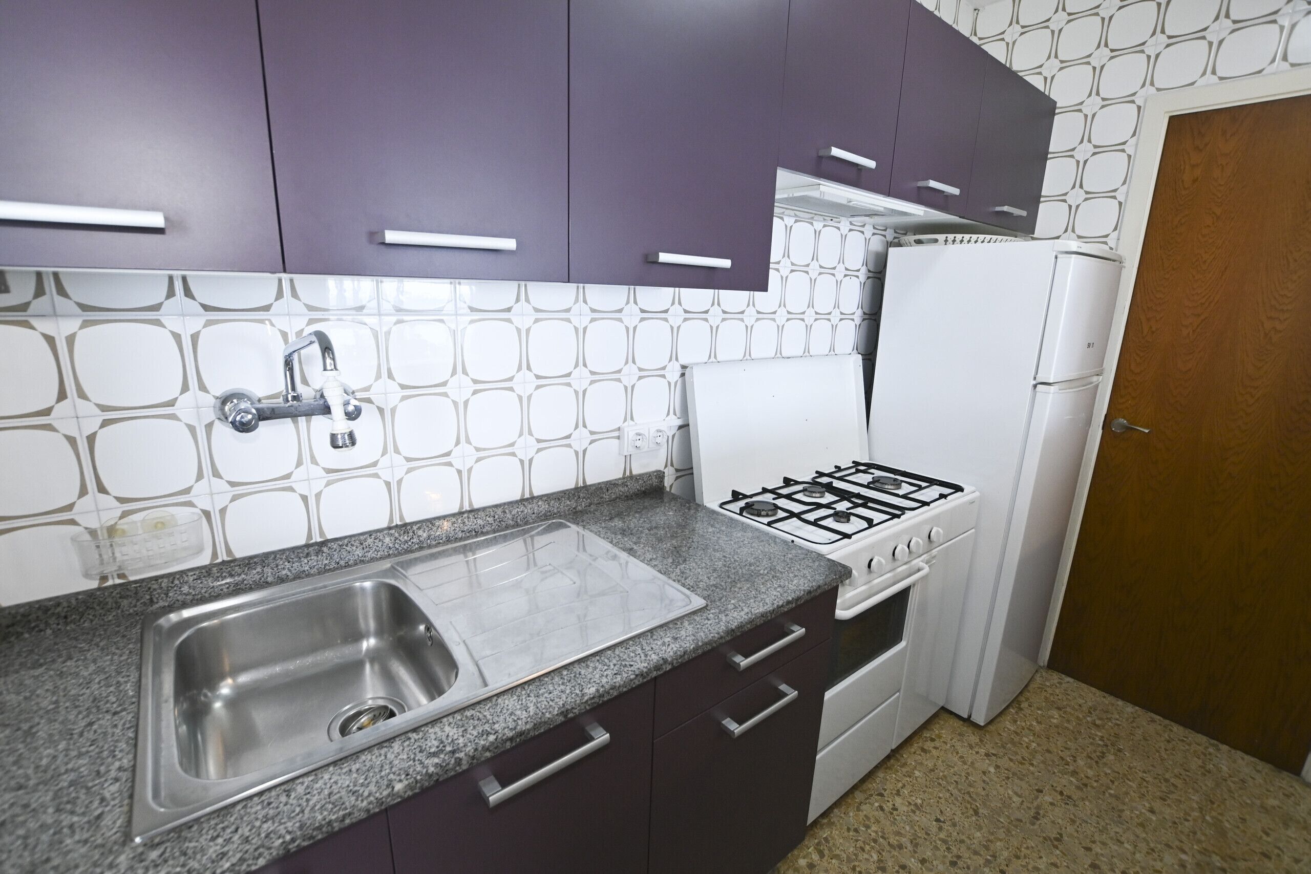 A kitchen with a granite countertop, stainless steel sink, white gas stove, and a white refrigerator.