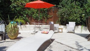 An outdoor patio with a dining table, chairs, a red umbrella, and a large planter. - Villa Marjolette (Cannes)