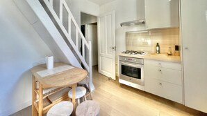 A modern kitchen with white cabinets, a gas stove, and a wooden dining table with chairs. - Villa Marjolette (Cannes)