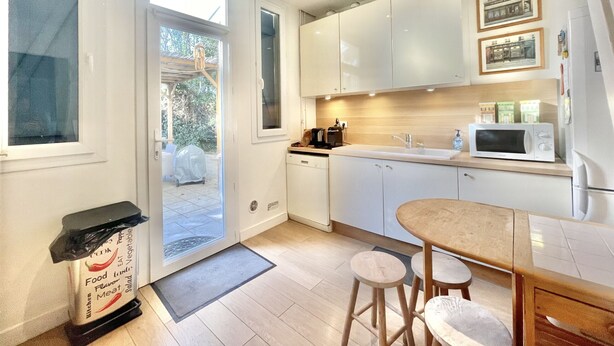 A modern kitchen with white cabinets, a microwave, and a dining area with stools. - Villa Marjolette (Cannes)