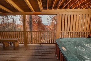A wooden deck with a hot tub and a bench, overlooking a forest with autumn foliage. - Arcade Games, Pool Table, FREE access to Pool and Putt Putt, 5 miles to town (Sevierville)