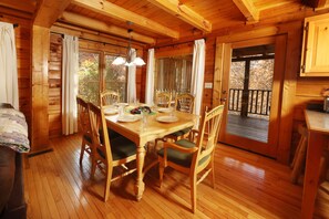 A wooden cabin interior with a dining table set for four, surrounded by wooden chairs with green cushions. - Arcade Games, Pool Table, FREE access to Pool and Putt Putt, 5 miles to town (Sevierville)