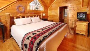 Camera da letto in una baita di legno, con un letto, una televisione e una finestra decorata con un festone.
