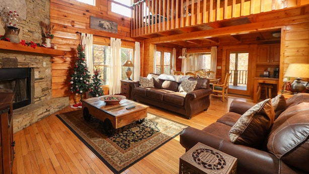 Un accogliente interno di una baita in legno, con camino, pavimento in legno, divano in pelle e un abete decorato per Natale.