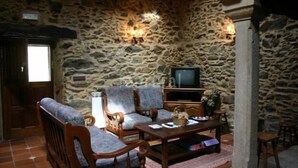 Ein Wohnzimmer mit steinernen Wänden, einer Couch, Sesseln, einem Couchtisch und einem Fernseher.