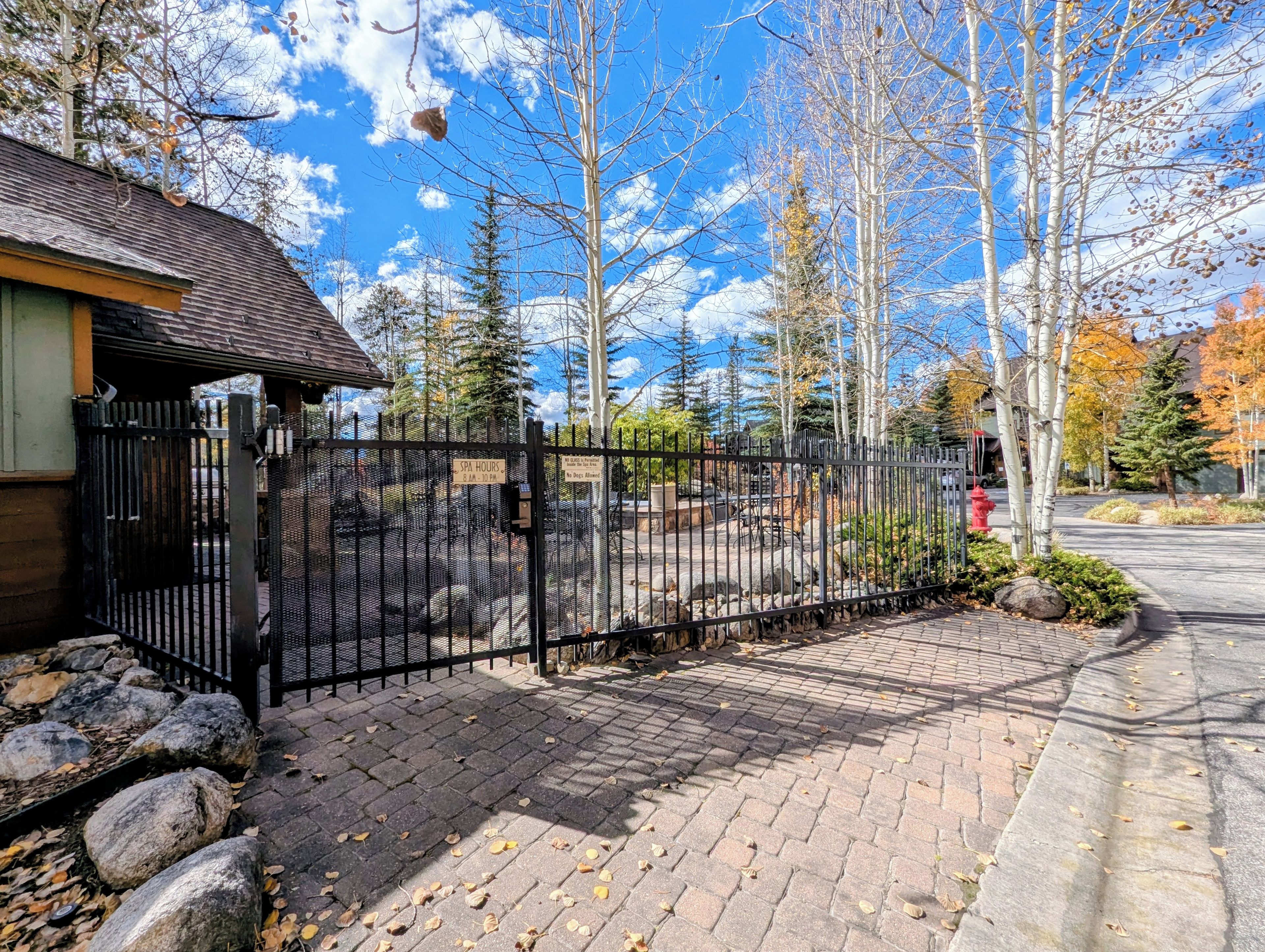 A gated entrance with a paved pathway, a red fire hydrant, and leaf-covered ground.