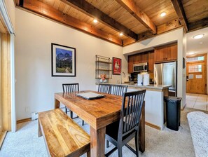 A dining area with a wooden table and chairs, a kitchen with modern appliances, and a wooden ceiling.