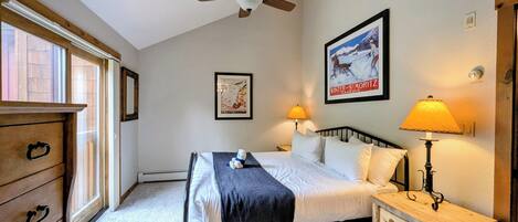 Une chambre à coucher comprenant un lit, une commode en bois, une table de chevet avec une lampe, un ventilateur de plafond et deux tableaux encadrés accrochés au mur.