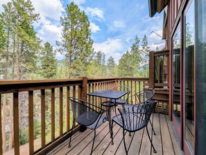 A wooden deck with a table and chairs, overlooking a forested area.