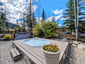 A hot tub surrounded by a wooden deck, a stone planter with flowers, and a mountain backdrop. - Shuttle to Lifts/Walk to Lakeside Village, Hot Tub (Keystone)