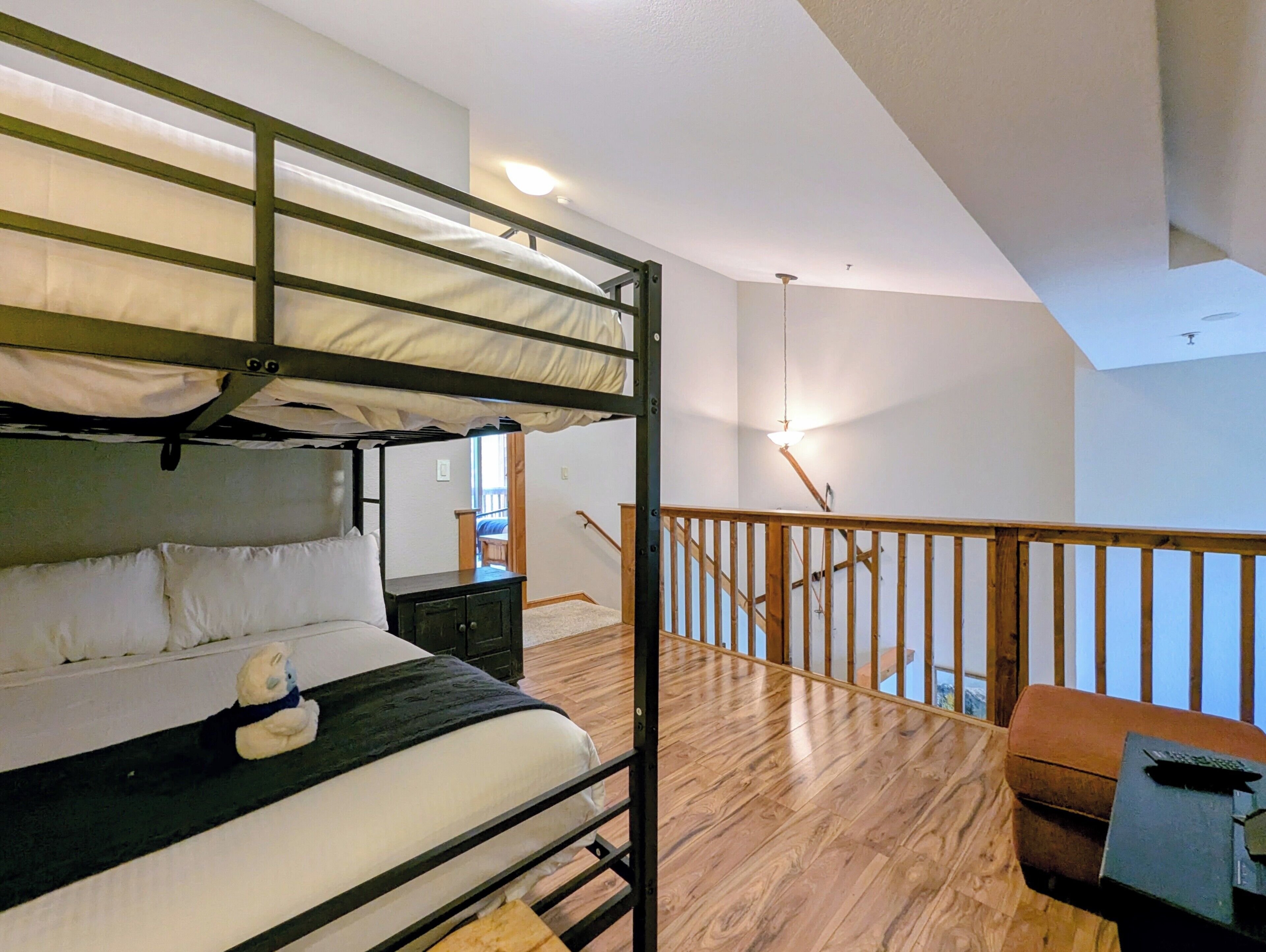 Una cama litera con un oso de peluche, un escritorio de madera y una escalera que lleva a un nivel superior.